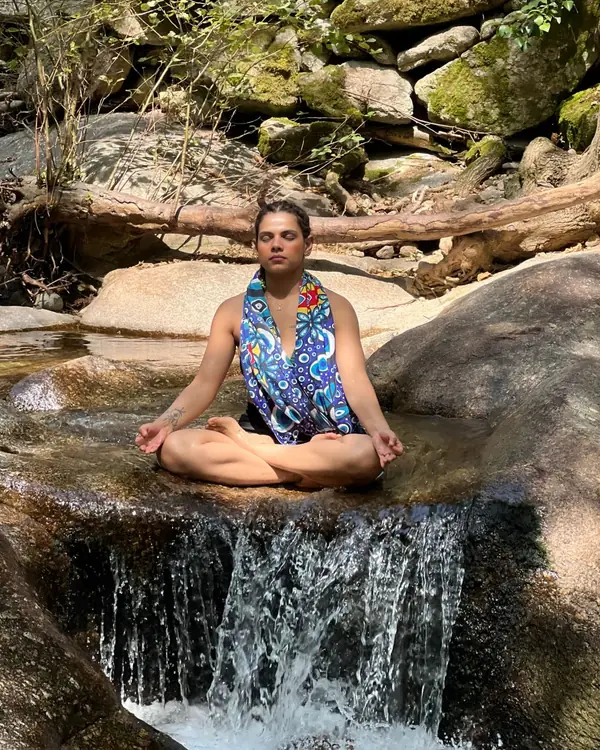 Deep Shikha meditando con las piernas cruzadas sobre una pequeña cascada