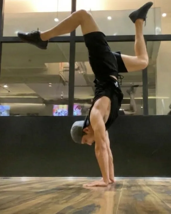 Keshav haciendo el pino con las piernas abiertas, en un estudio