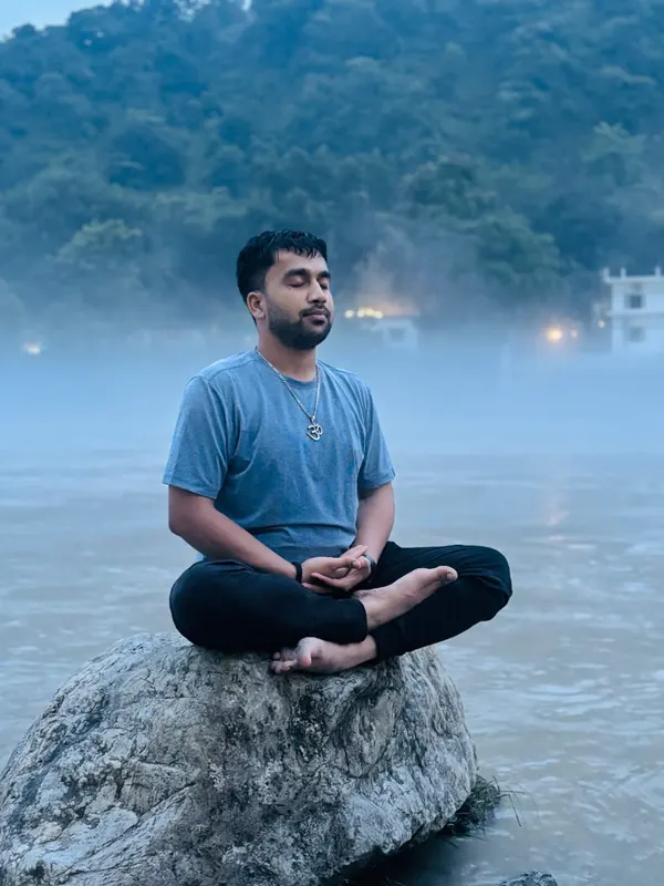 Yogacharye Vishal meditando sobre una roca junto a un río entre la niebla